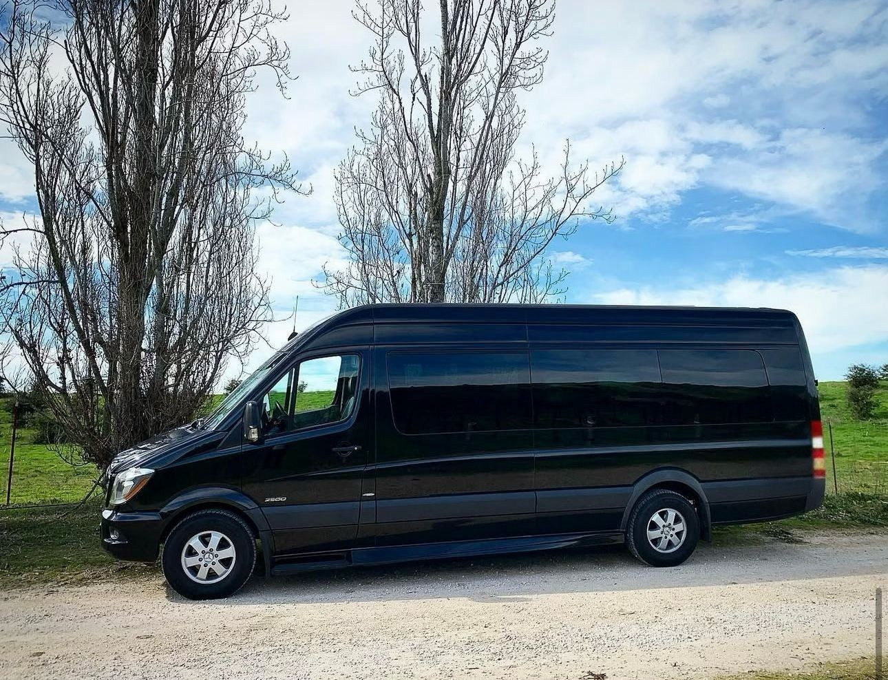 Rear view of a black luxury SUV used for limo service Santa Barbara, parked in an outdoor lot with surrounding greenery.